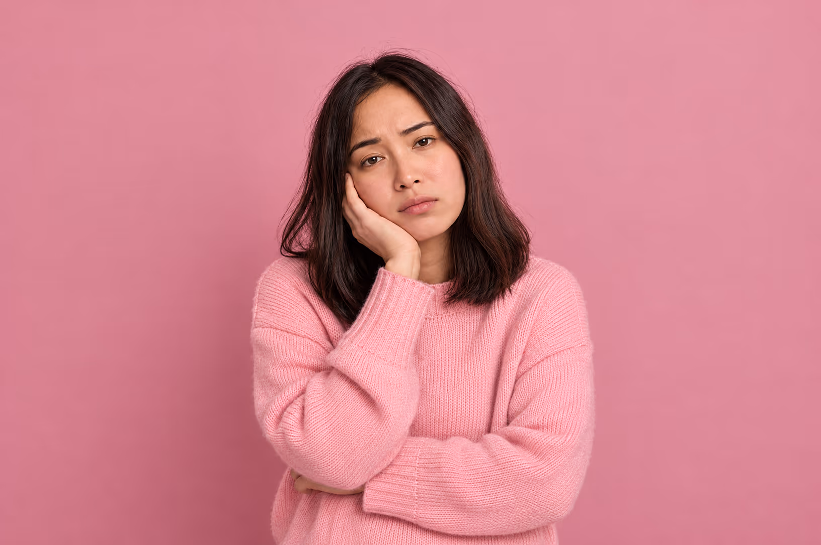 A woman in a pink sweater resting her face in her hand, tired