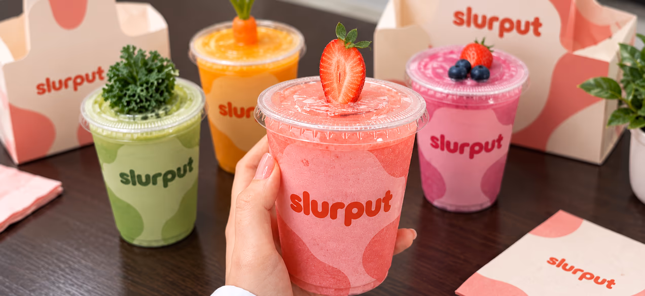 Four Slurput smoothies in green, orange, pink and berry on a dark table